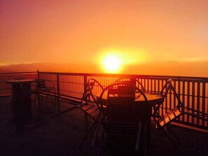 Ein Sonnenuntergangsblick von einem Balkon mit Stühlen und einem Tisch.