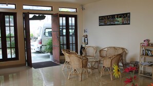 An open doorway leading outside, a rattan table with chairs, a bookshelf, and a painting on the wall. - Pure Nature Hotel (Kandy)