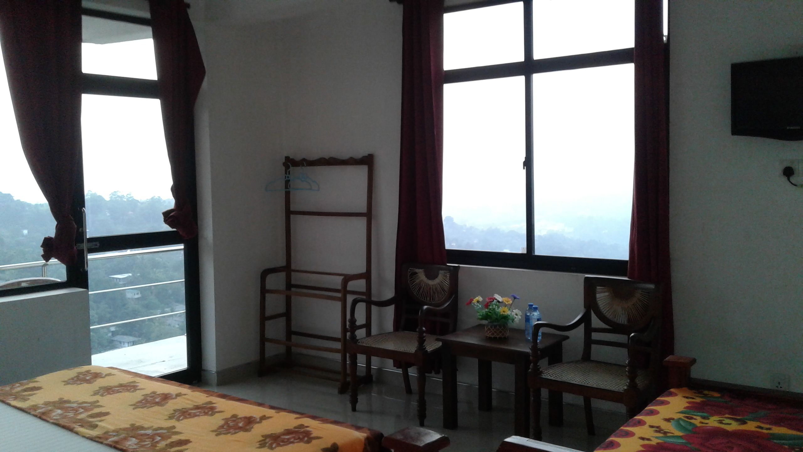 A room with a bed, two chairs, a small table with a vase of flowers, and a window with a view of a mountainous landscape.