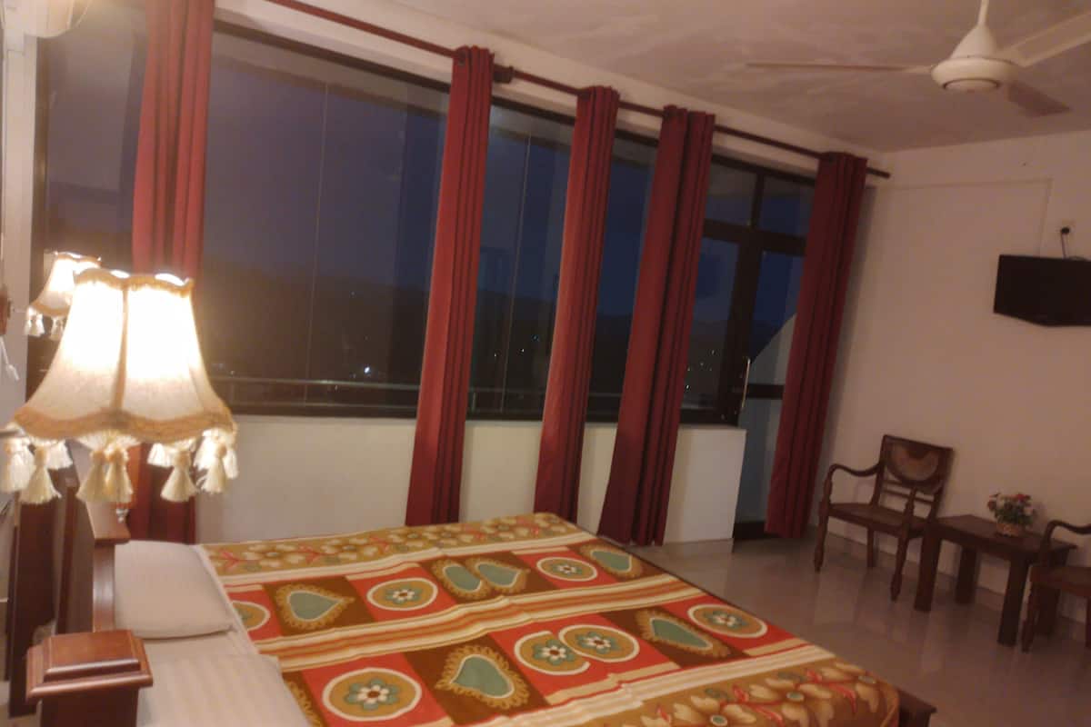 A hotel room with a bed, a desk, a chair, a TV, and a window with curtains.