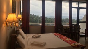 A hotel room with a bed, a desk, and a view of a mountainous landscape through large windows. - Pure Nature Hotel (Kandy)