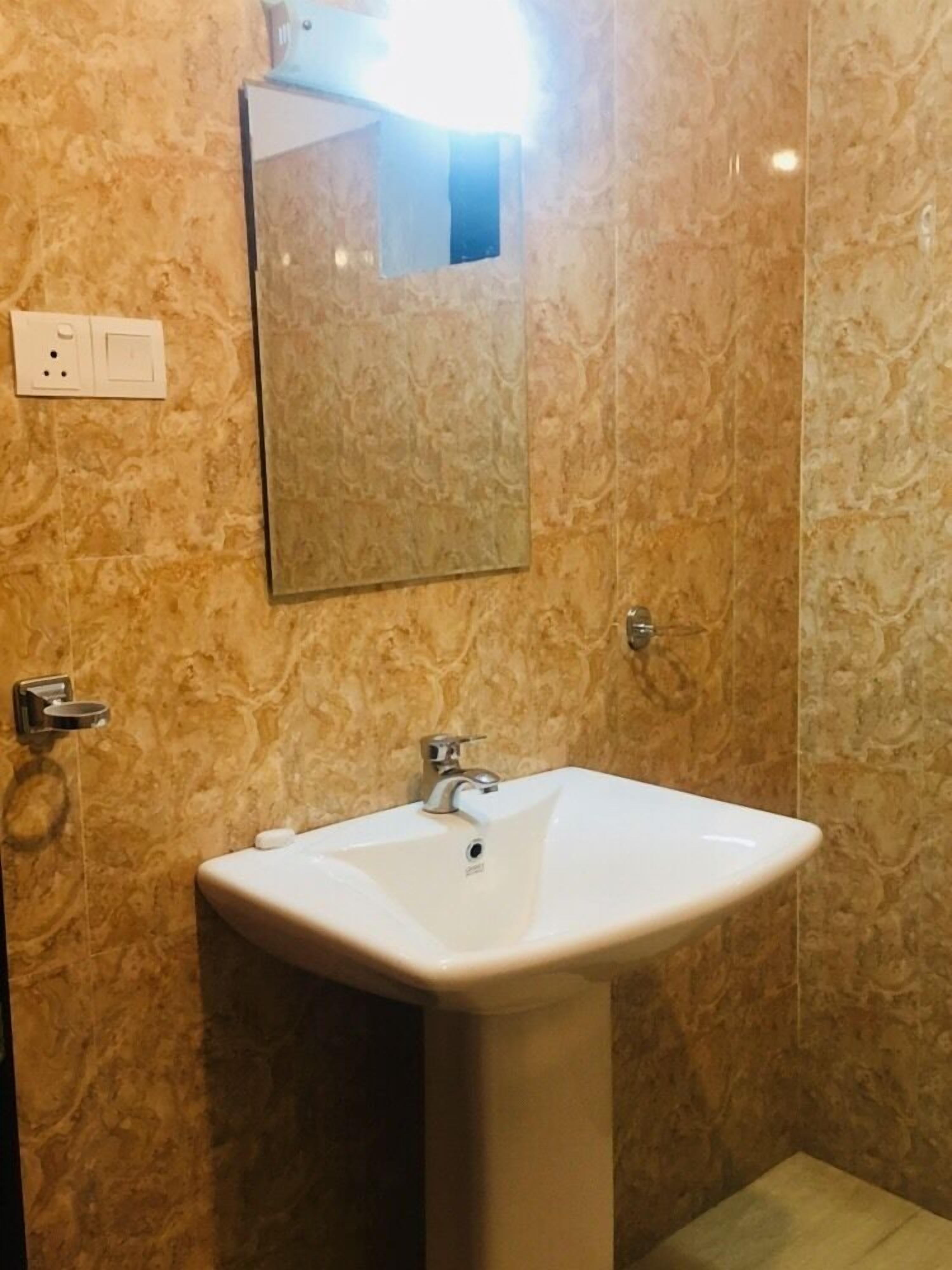 A bathroom with a white sink, a mirror, and a wall-mounted light fixture.