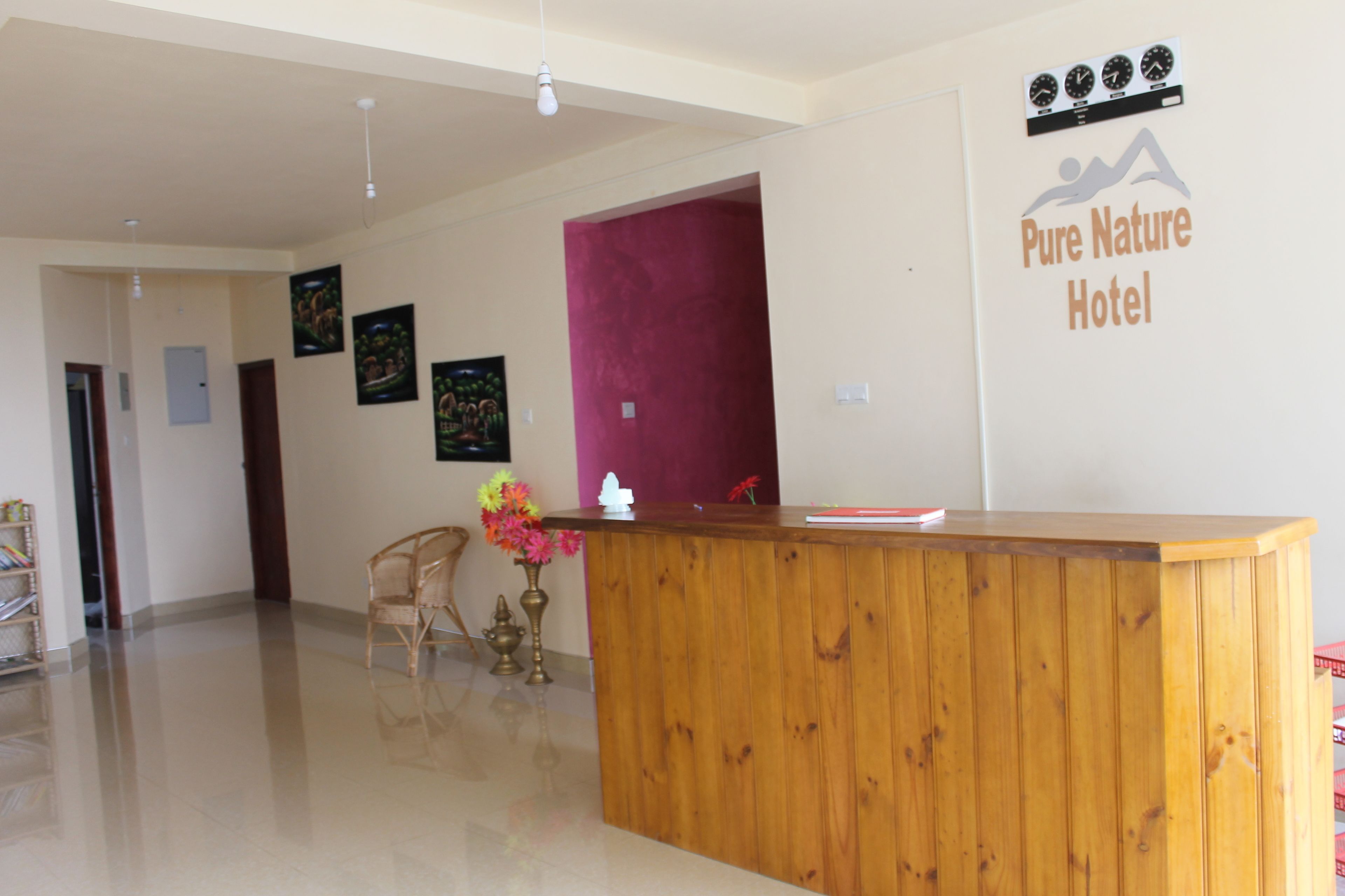 A hotel reception desk with a wooden counter, a reception area with a red accent wall, and a sign for 'Pure Nature Hotel'.