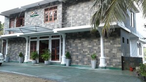 A building with a stone facade, a covered entrance with glass doors, and potted plants. - Pure Nature Hotel (Kandy)