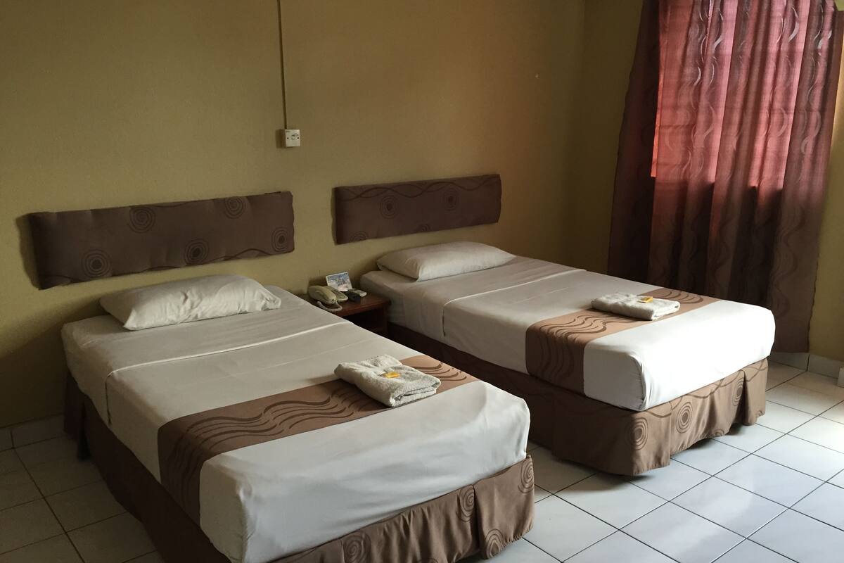A hotel room with two beds, each with a headboard, bedside tables, and a telephone.