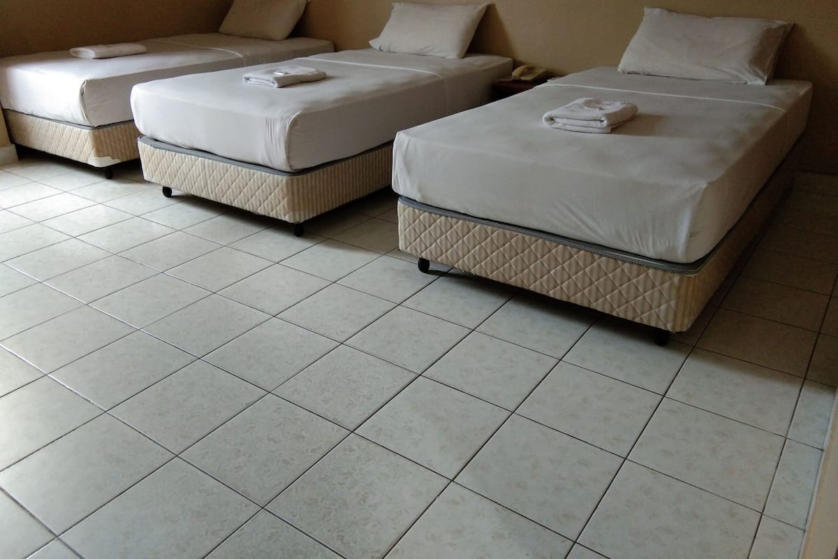 A hotel room with three single beds, each with a pillow and a folded towel.
