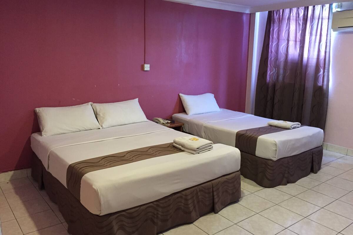 A hotel room with two beds, a telephone on the nightstand, and a window with curtains.