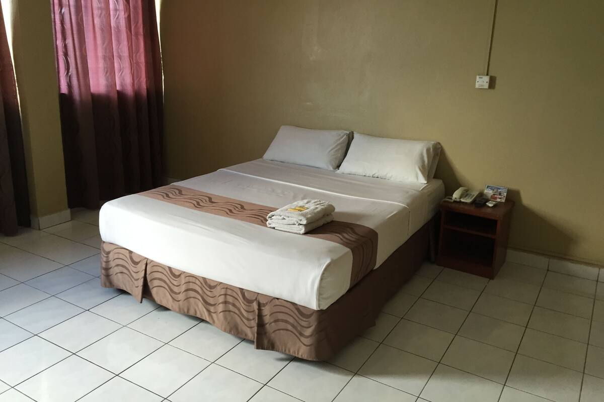A hotel room with a bed, a nightstand, a telephone, and a folded towel.