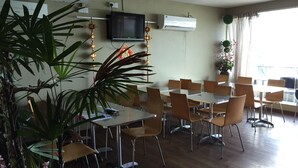 Un comedor con mesas, sillas, un televisor, un equipo de aire acondicionado y plantas en macetas.