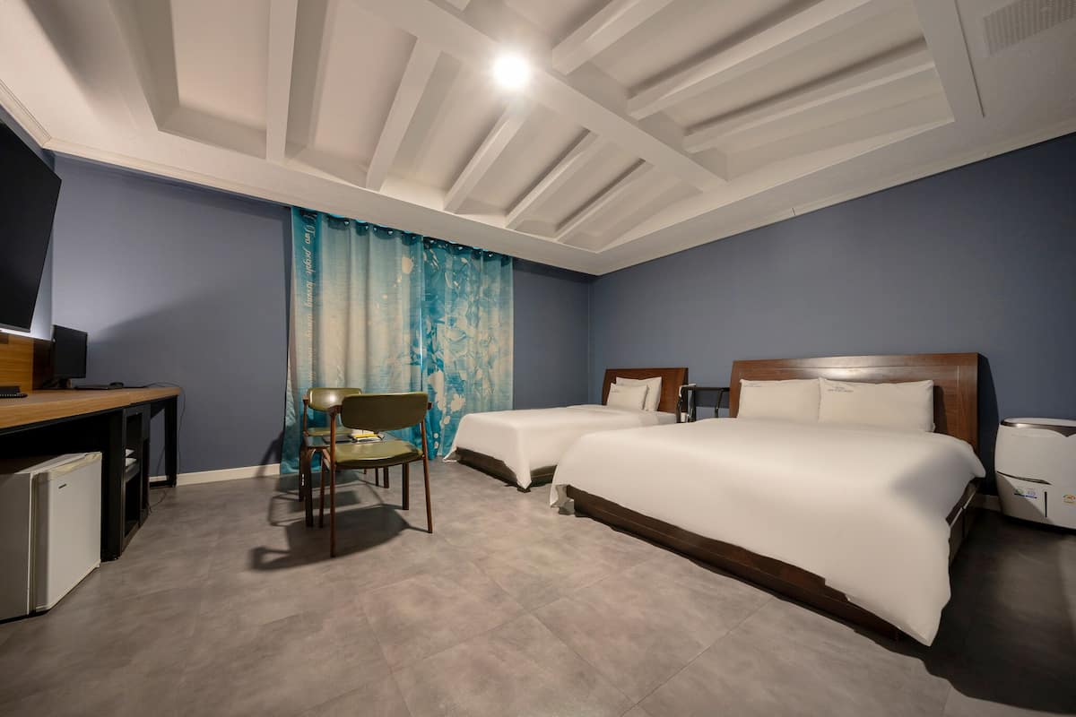 A hotel room with two beds, a desk with a computer, a chair, and a small refrigerator.