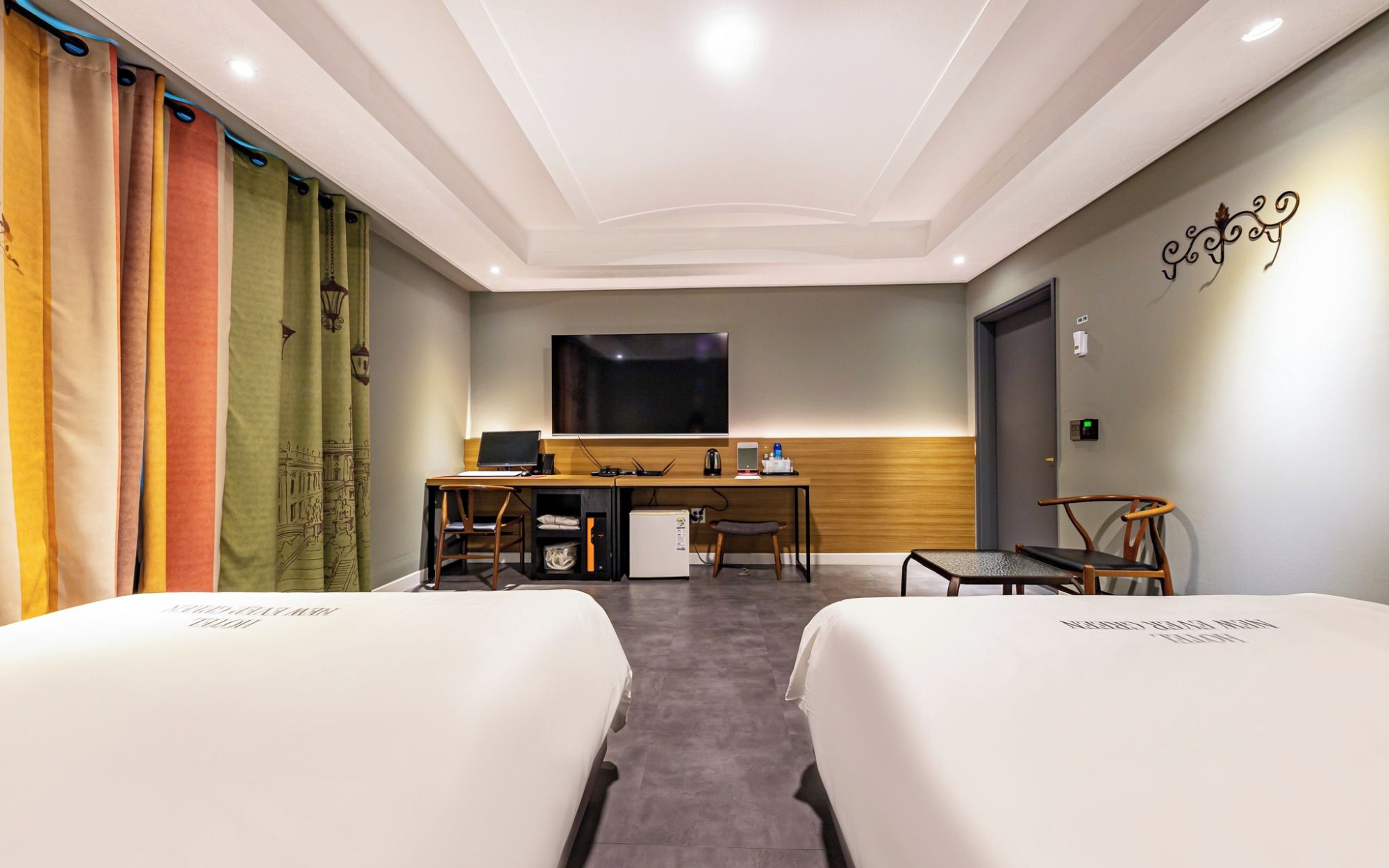 A hotel room with two beds, a desk, a television, and a small kitchenette.