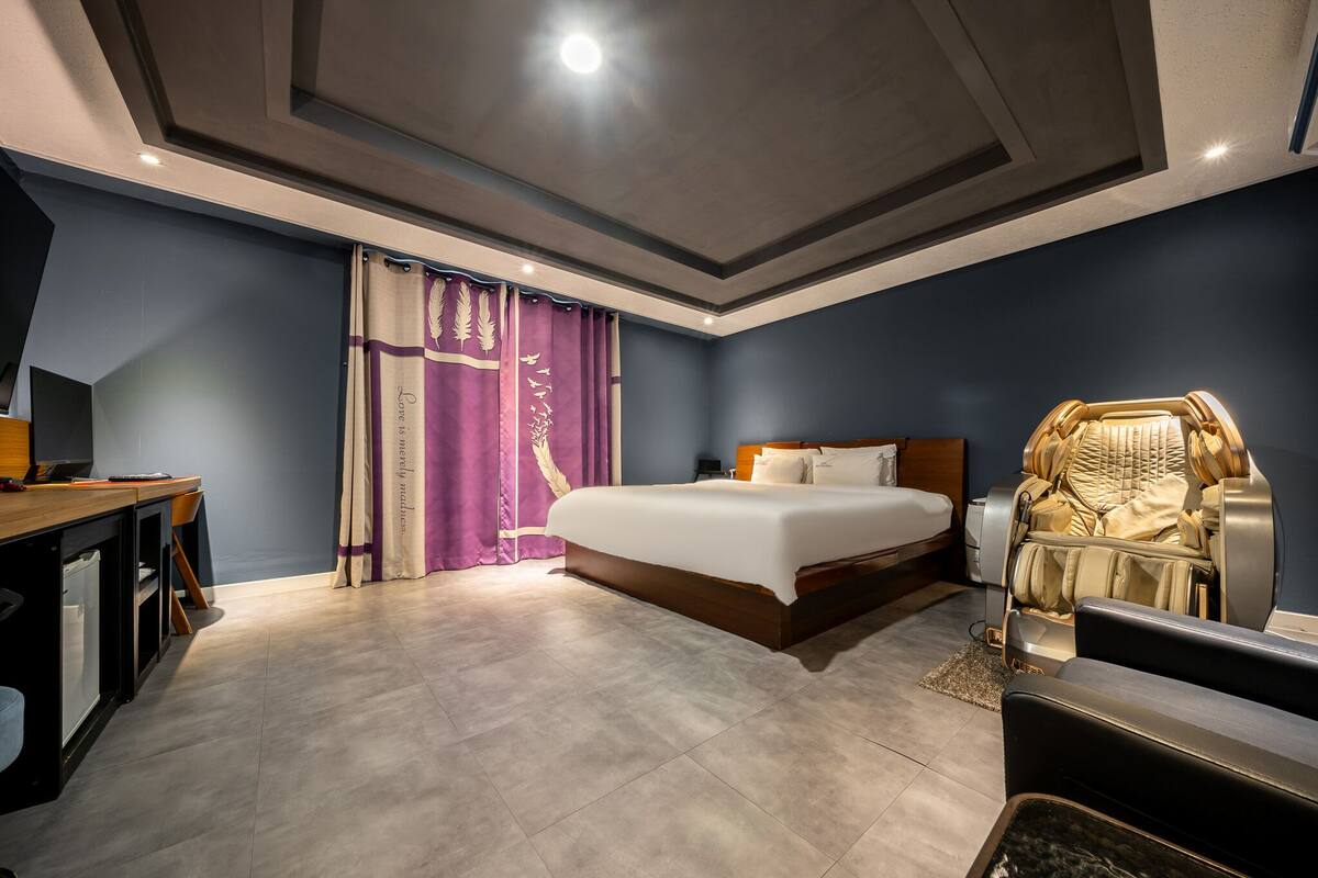 A modern hotel room with a large bed, a desk, and a massage chair.