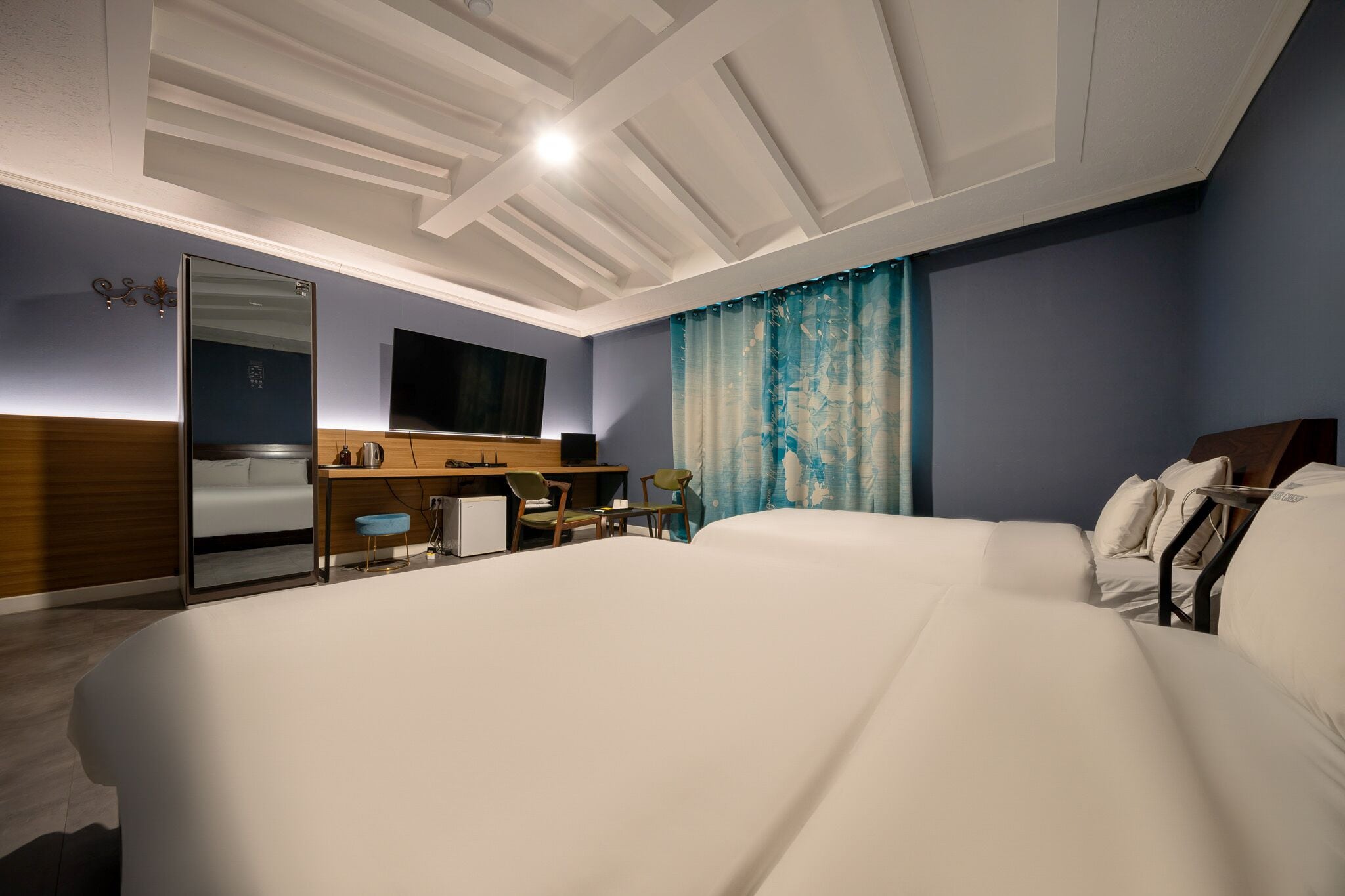 Una habitación de hotel moderna con una cama grande, un escritorio con una computadora, un espejo y un televisor.