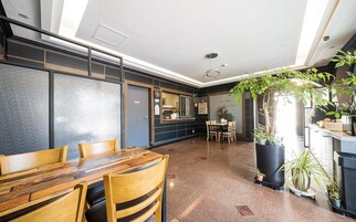 Un comedor moderno con una mesa y sillas de madera, una pared negra con un tablero de menú y plantas en macetas.