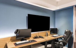 Una oficina moderna con dos escritorios, cada uno con monitor de computadora, teclado y ratón. Hay dos altavoces, una cafetera y una silla.