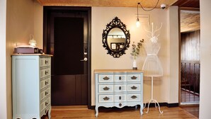 A room with a wooden ceiling, a dark door, a light blue dresser with multiple drawers, a large mirror, and a white floor lamp. - The One Hostel (Seoul)