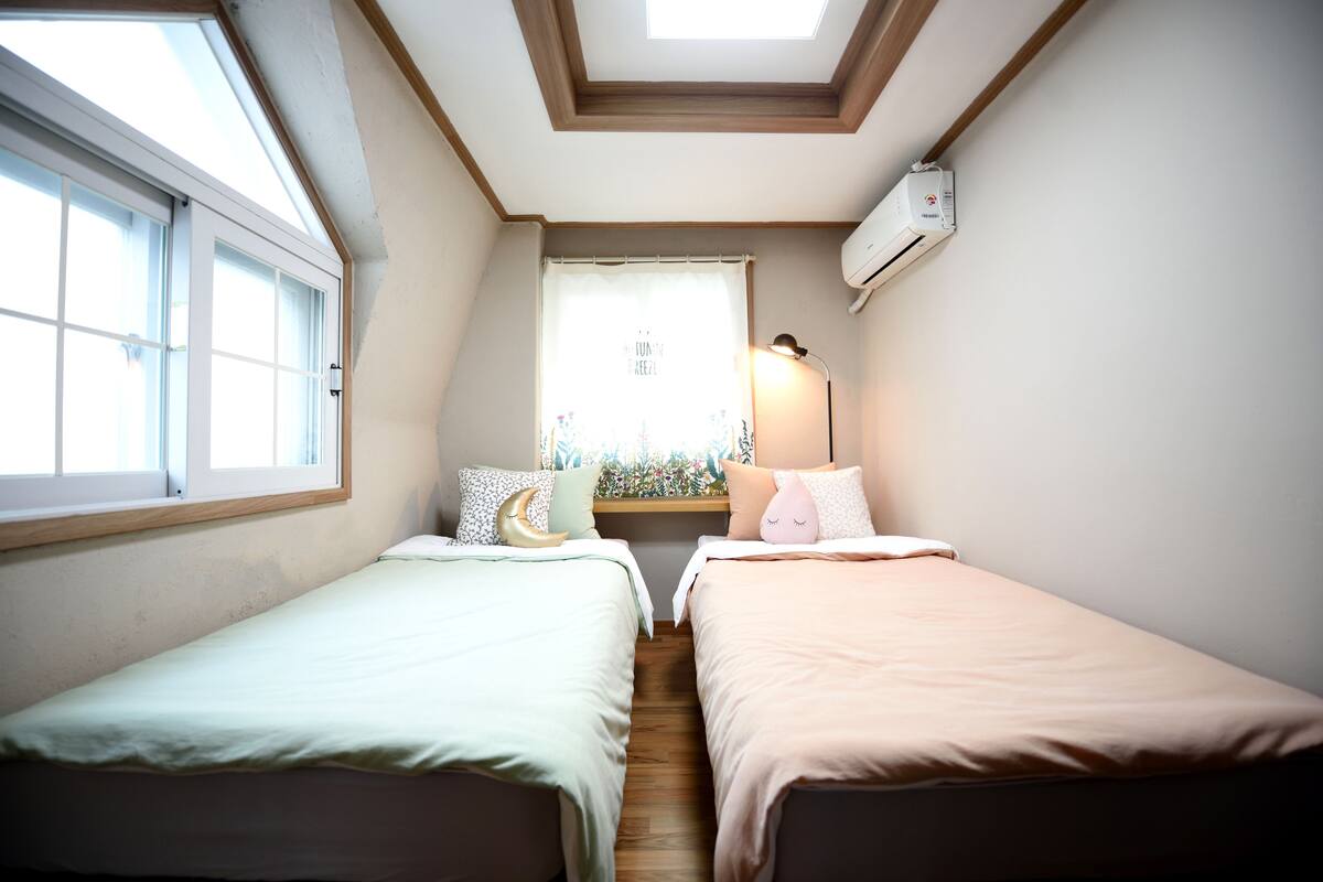 A bedroom with two beds, a skylight, a window, and an air conditioning unit.