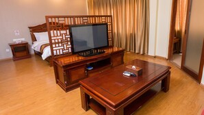 Habitación de hotel con cama de madera, televisor sobre un mueble de madera, una mesita de café y una cortina.
