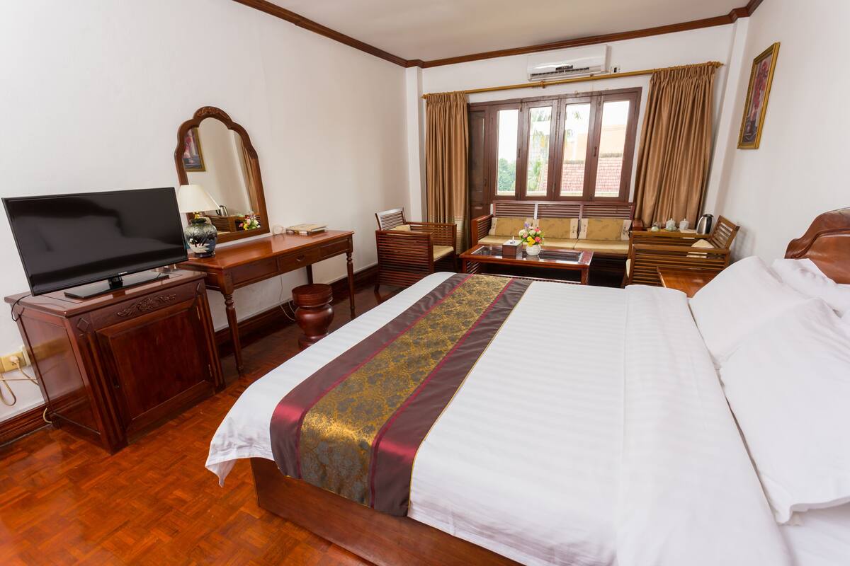 Een hotelkamer met een groot bed, een bureau met een televisie, een stoel, een raam met gordijnen en een houten vloer.