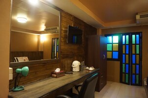 A room with a wooden desk, a large mirror, a television mounted above the desk, and a colorful stained glass door.