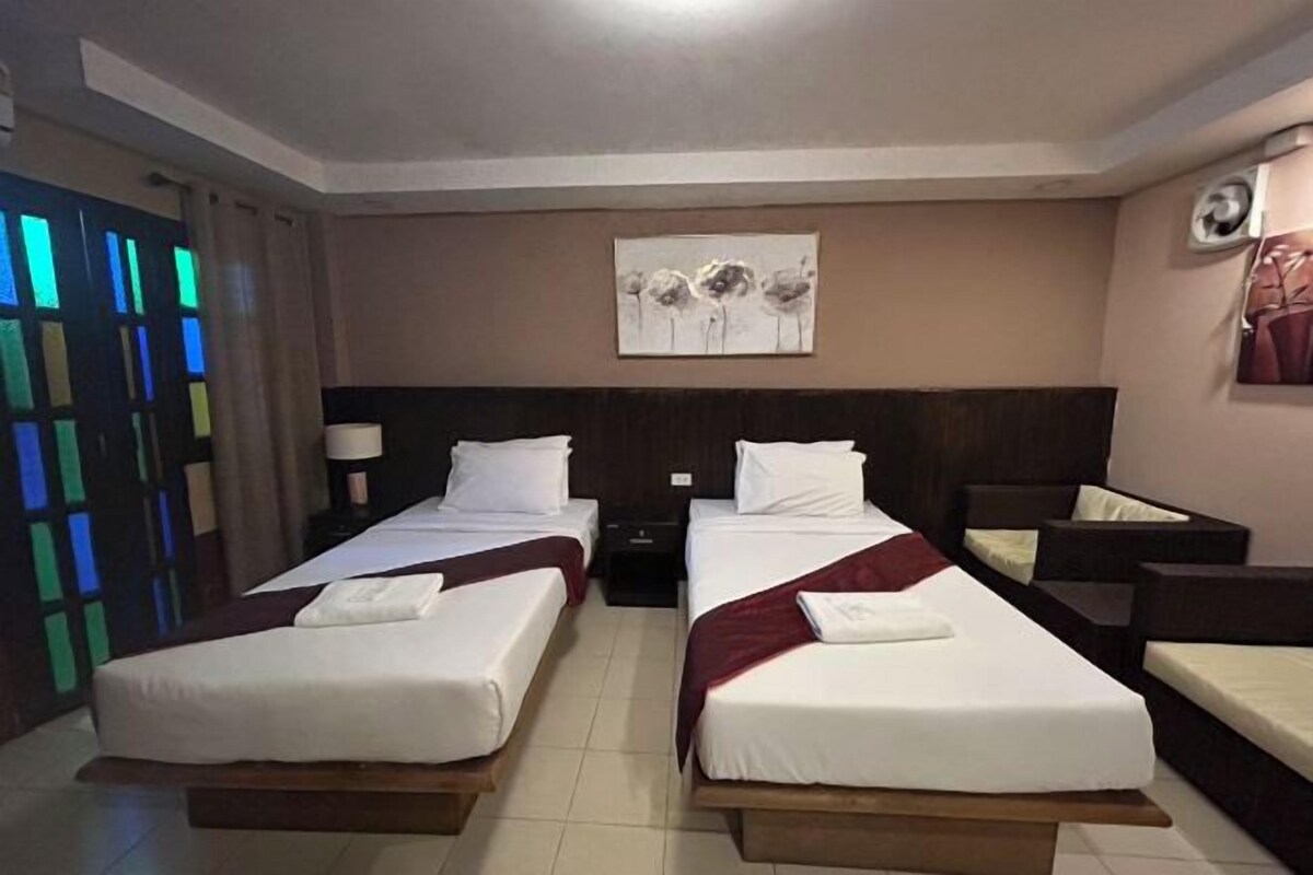 Habitación de hotel con dos camas individuales, una mesita de noche, una obra de arte colgada en la pared y una ventana con vistas al exterior.