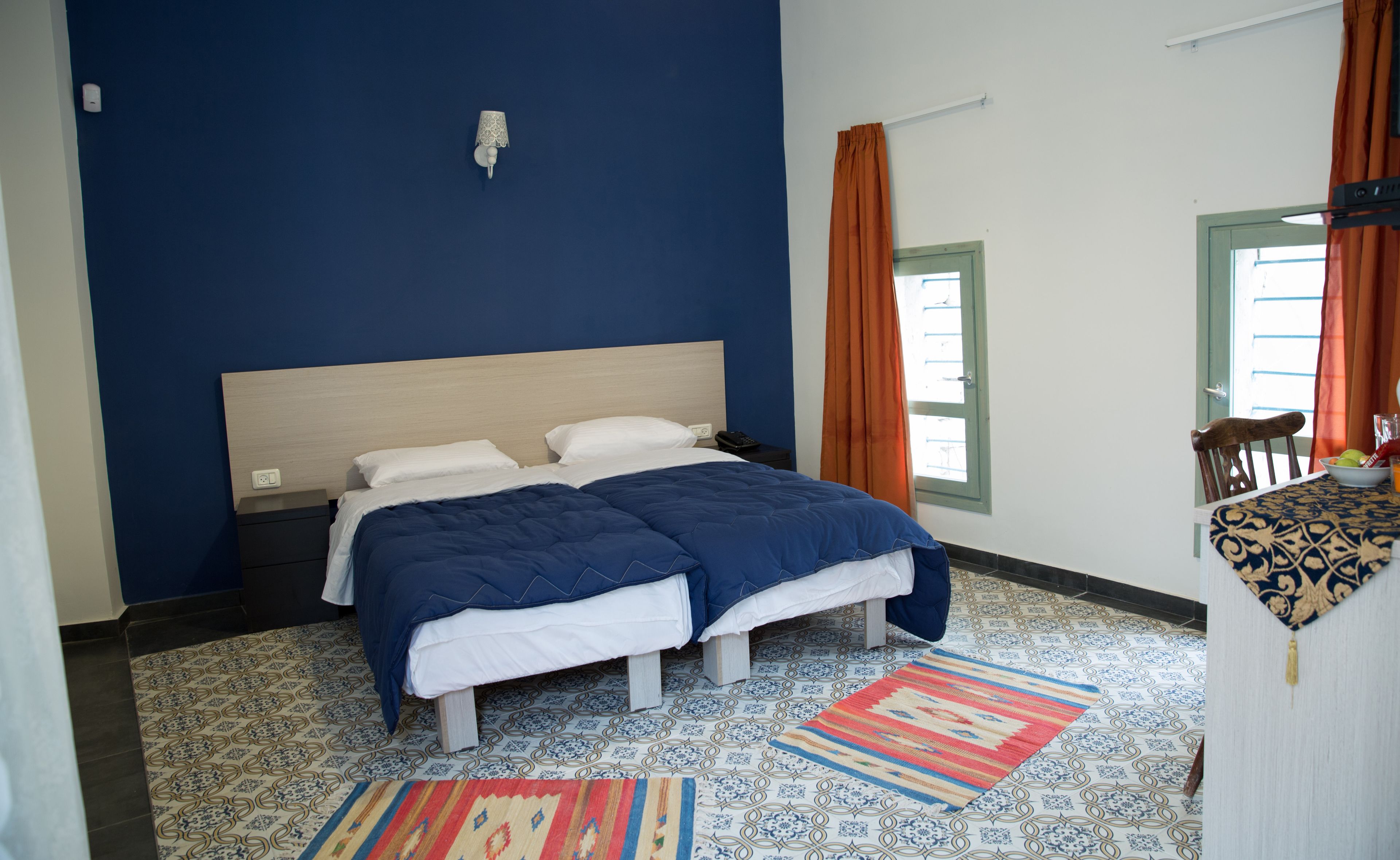 A bedroom with a bed, a nightstand, a lamp, a window with curtains, a chair, and a patterned rug.