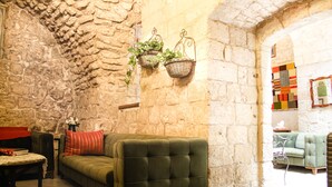 Un salon chaleureux avec un canapé vert, une petite table recouverte d’un plaid rouge et deux paniers suspendus contenant des plantes.