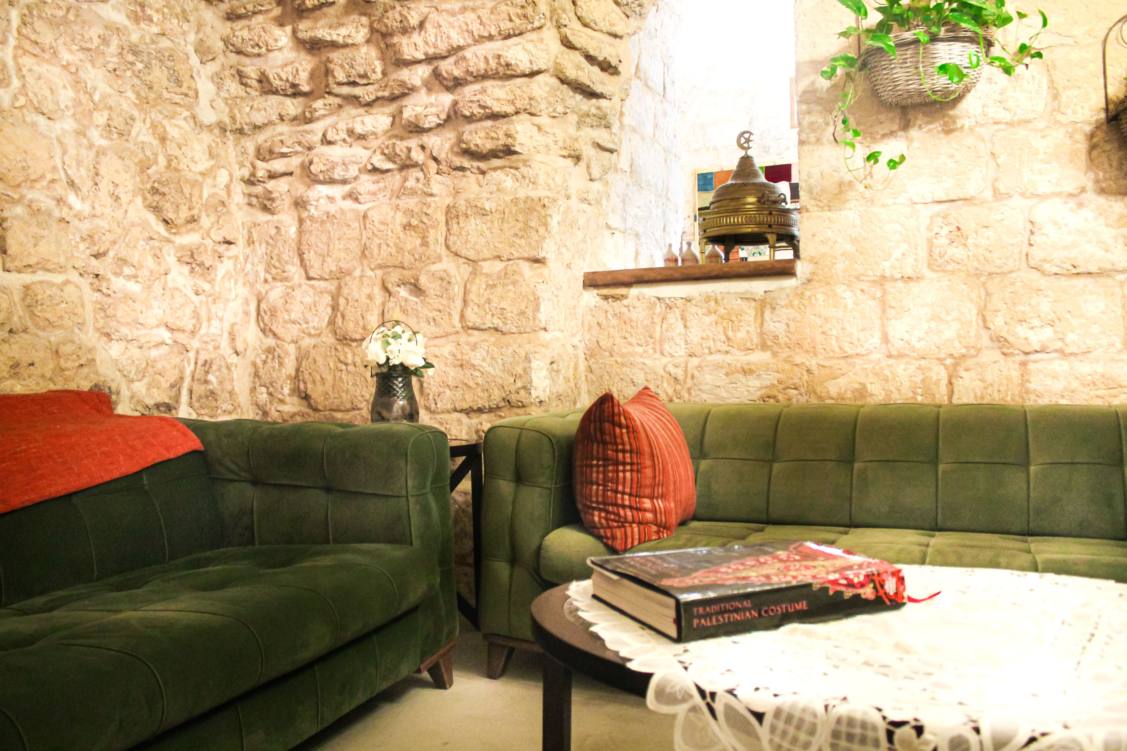 A cozy living room with a stone wall, green sofas, a small table with a book, and a hanging plant.