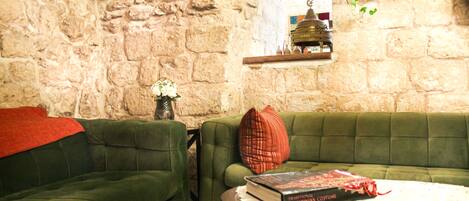 A cozy living room with a stone wall, green sofas, a small table with a book, and a hanging plant.