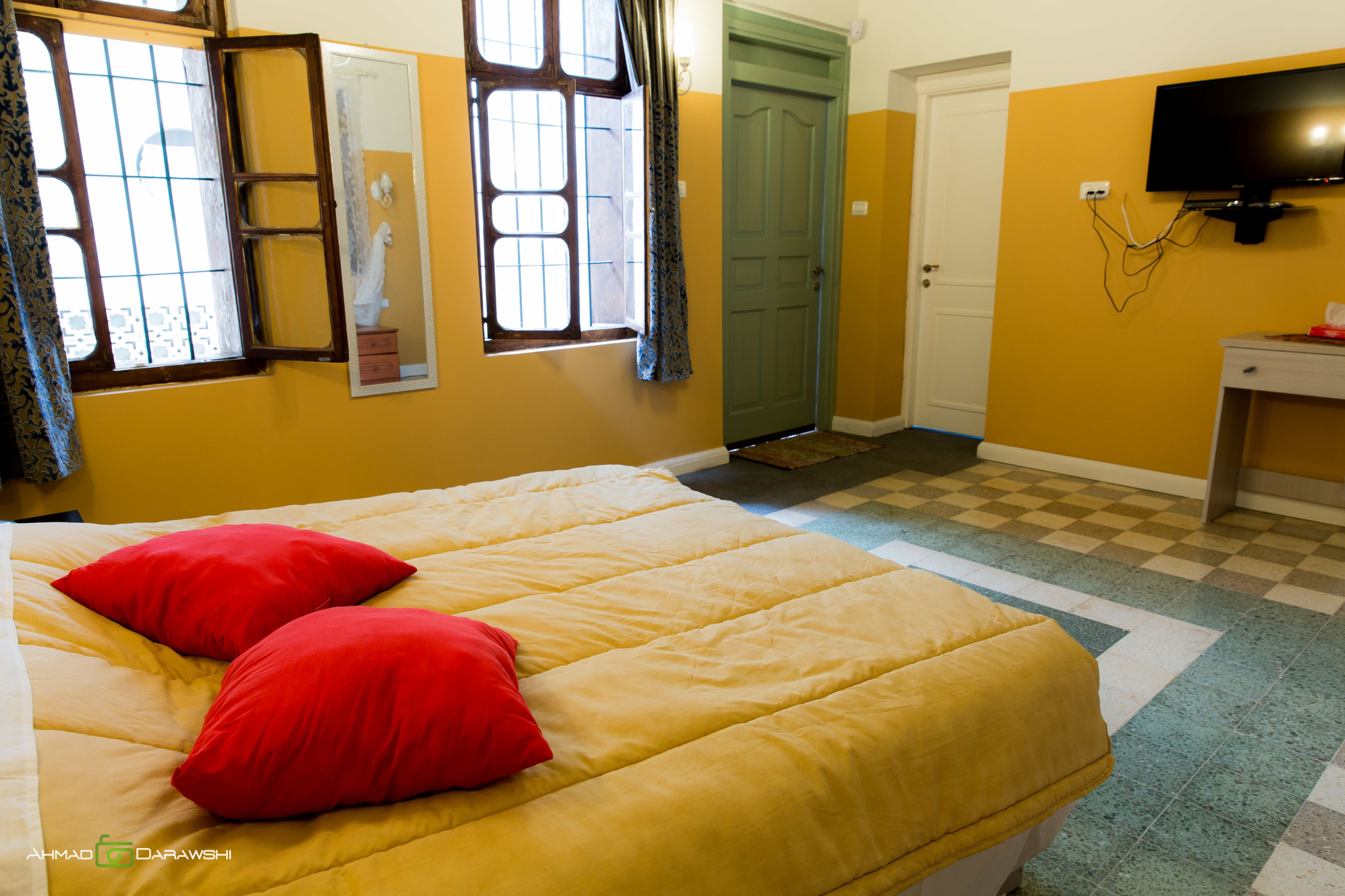 Un dormitorio con una cama, dos almohadas rojas, un espejo, un televisor y una puerta.
