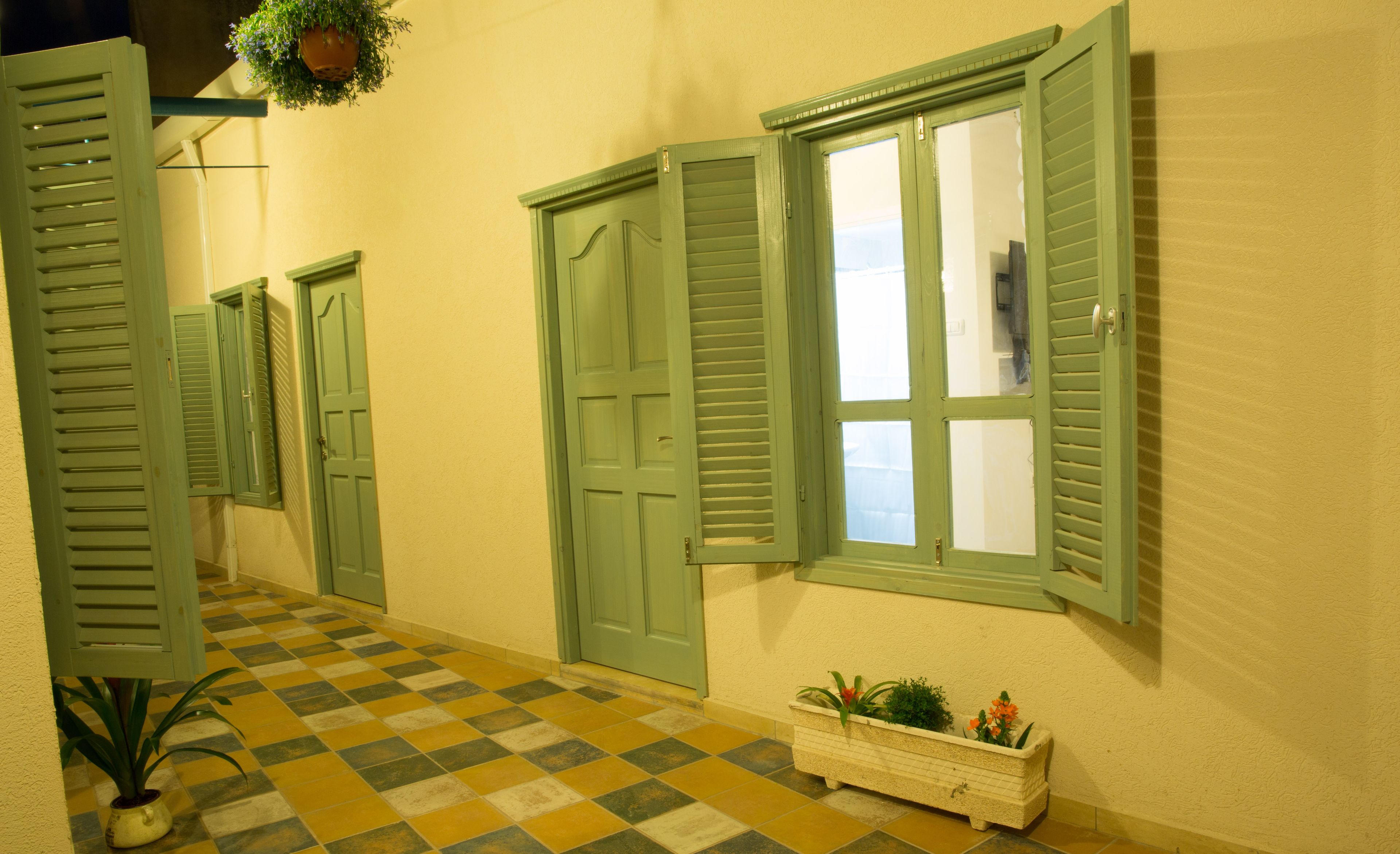 Un couloir avec des volets verts, un sol à carreaux et un bac à fleurs contenant des plantes.