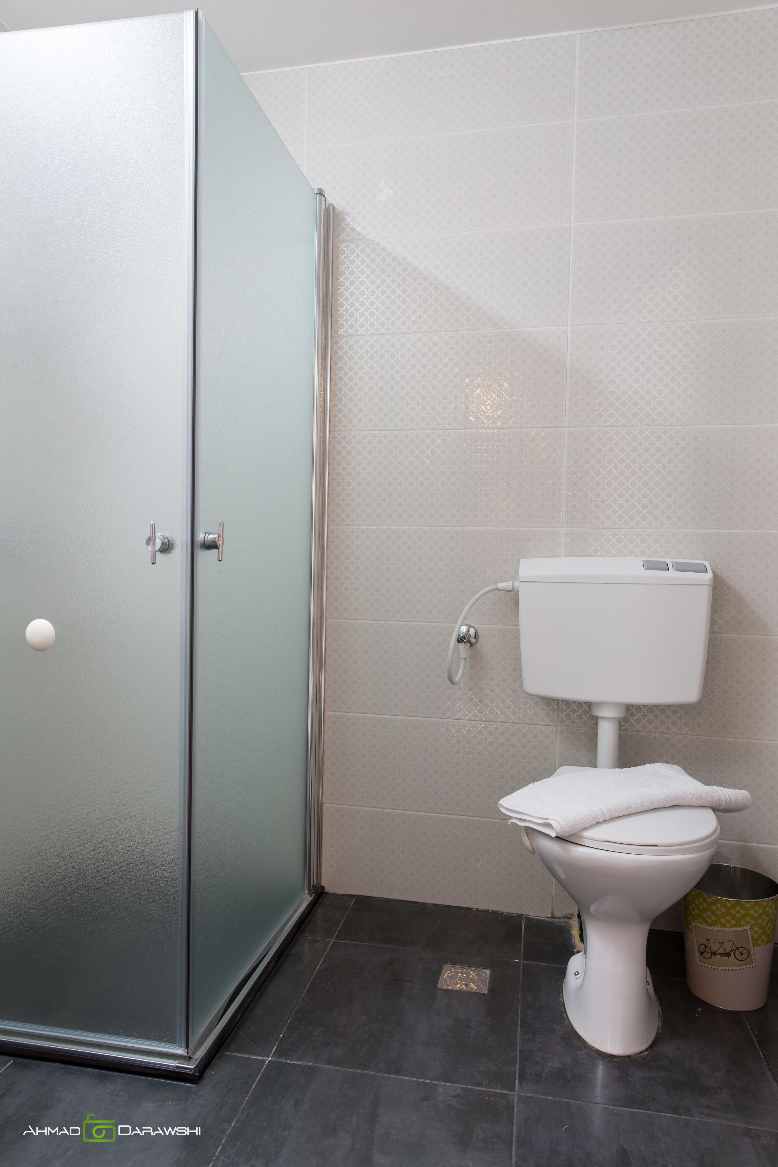 A bathroom with a toilet, a trash bin, and a shower area.