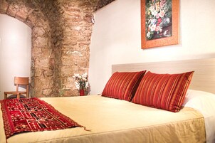 A bedroom with a stone wall, a bed with red and beige bedding, and a painting of flowers on the wall.