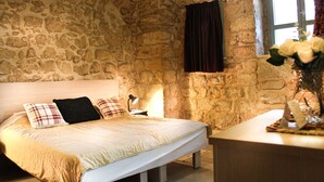 Une chambre avec un mur en pierre, un lit avec une tête de lit blanche, une table de chevet et une fenêtre avec des rideaux.