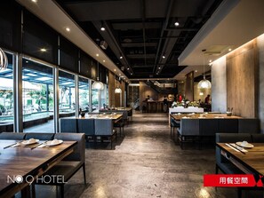 A modern hotel dining area with long tables and benches, large windows, and a central staircase.