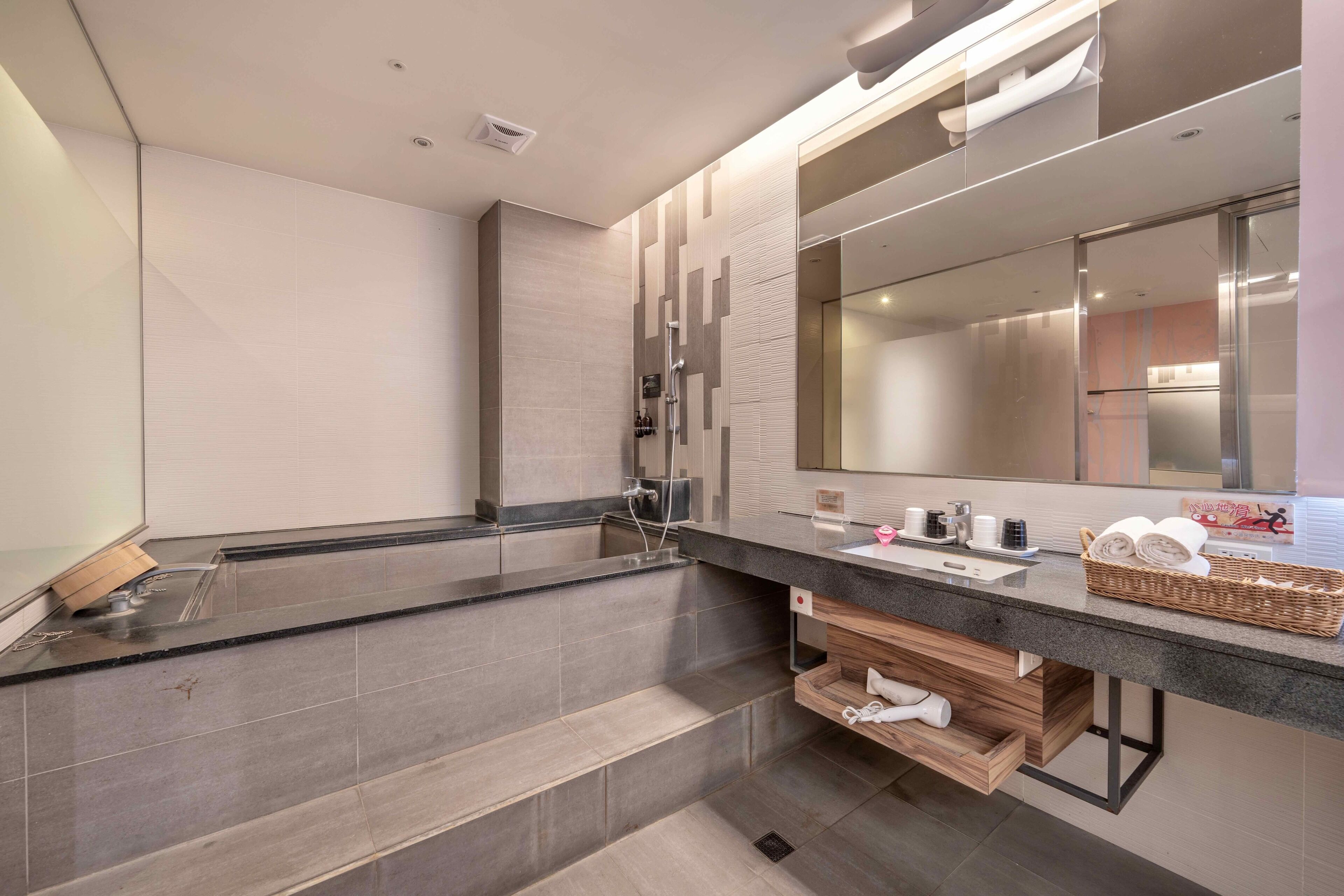 A modern bathroom with a large mirror, a bathtub, and a vanity with a sink and towel rack.