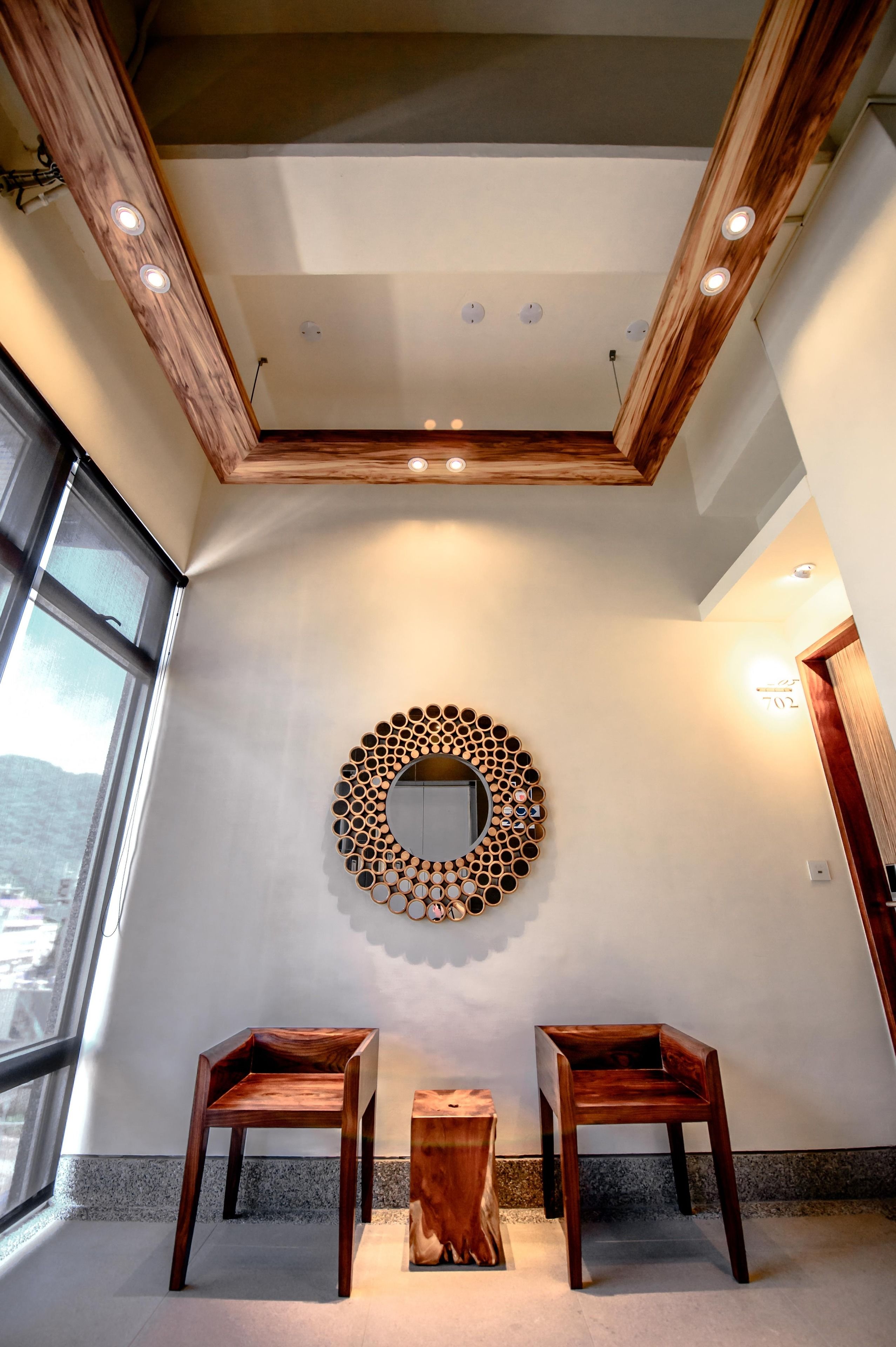 Un interior moderno con techo de madera, iluminación empotrada, un adorno circular en la pared y dos sillas de madera.