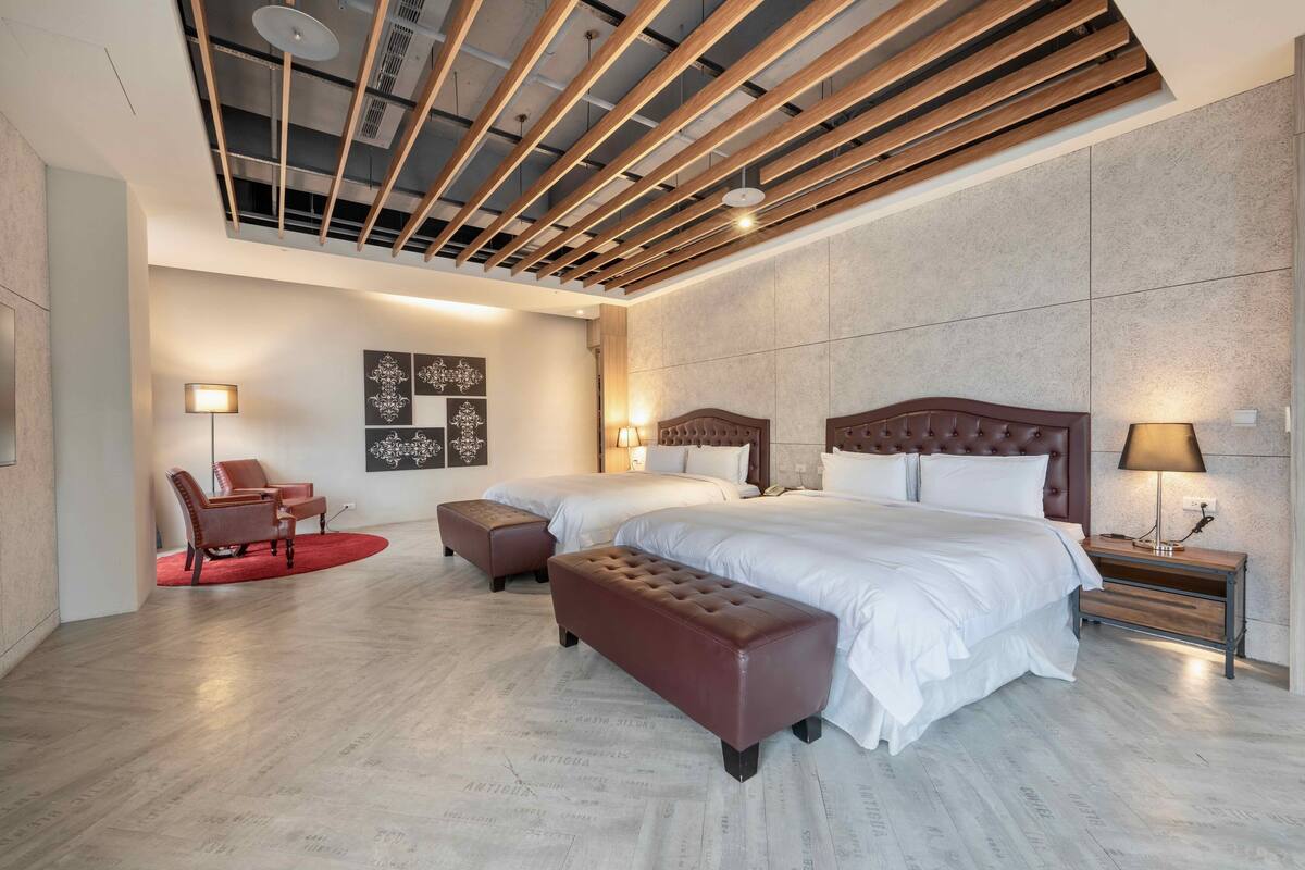 A modern hotel room with a large bed, two bedside tables, a red chair, and a bench.