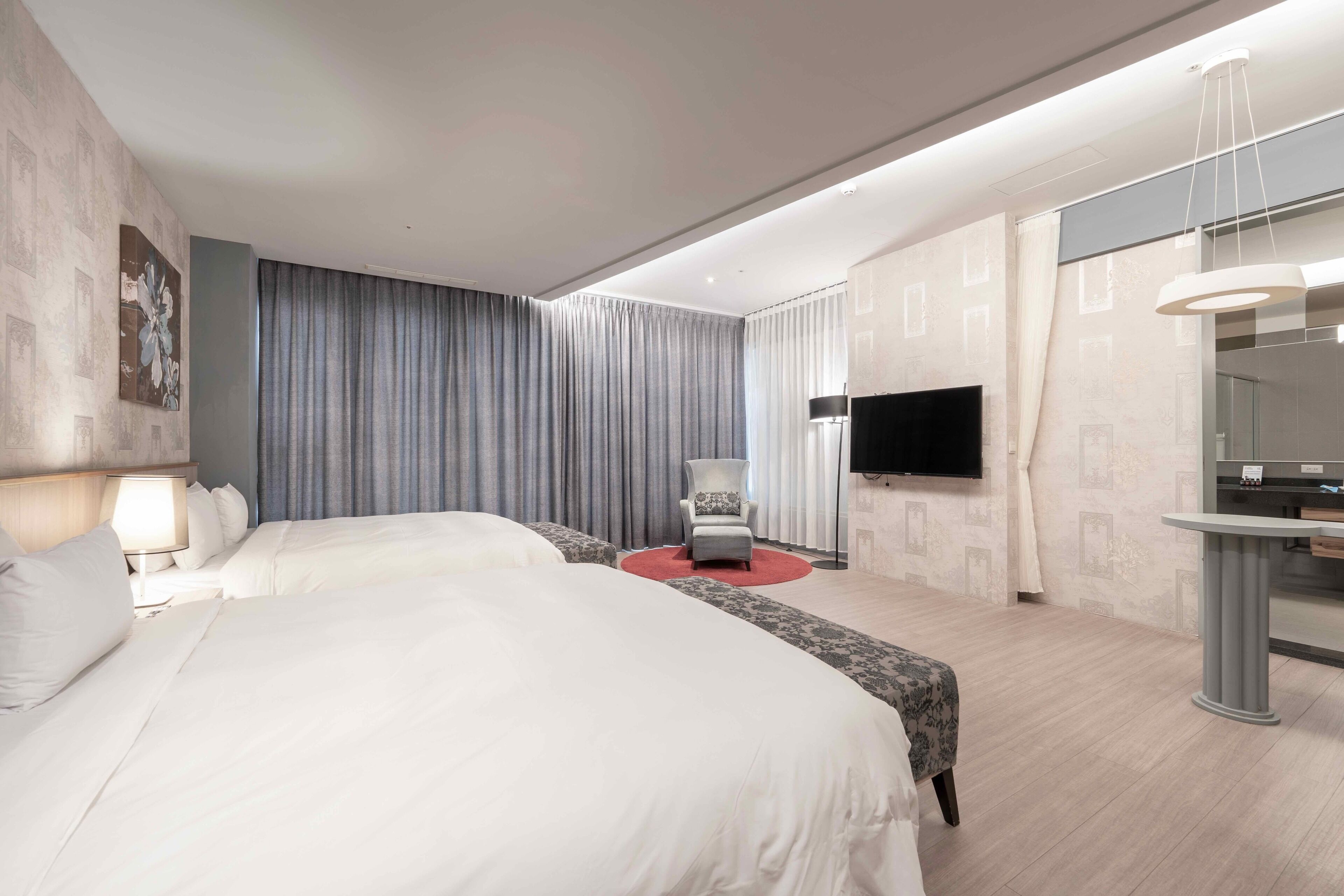 Ein modernes Hotelzimmer mit zwei Betten, einem Flachbildfernseher, einem Schreibtisch und einem Sessel.