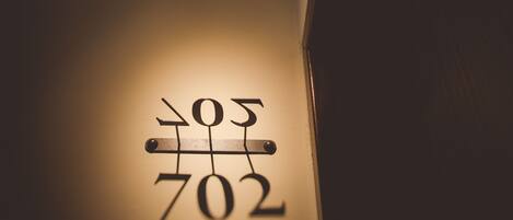 Ein an der Wand befestigtes Schild mit den leuchtenden Nummern „702“ und „505“ in einem schwach beleuchteten Gang.