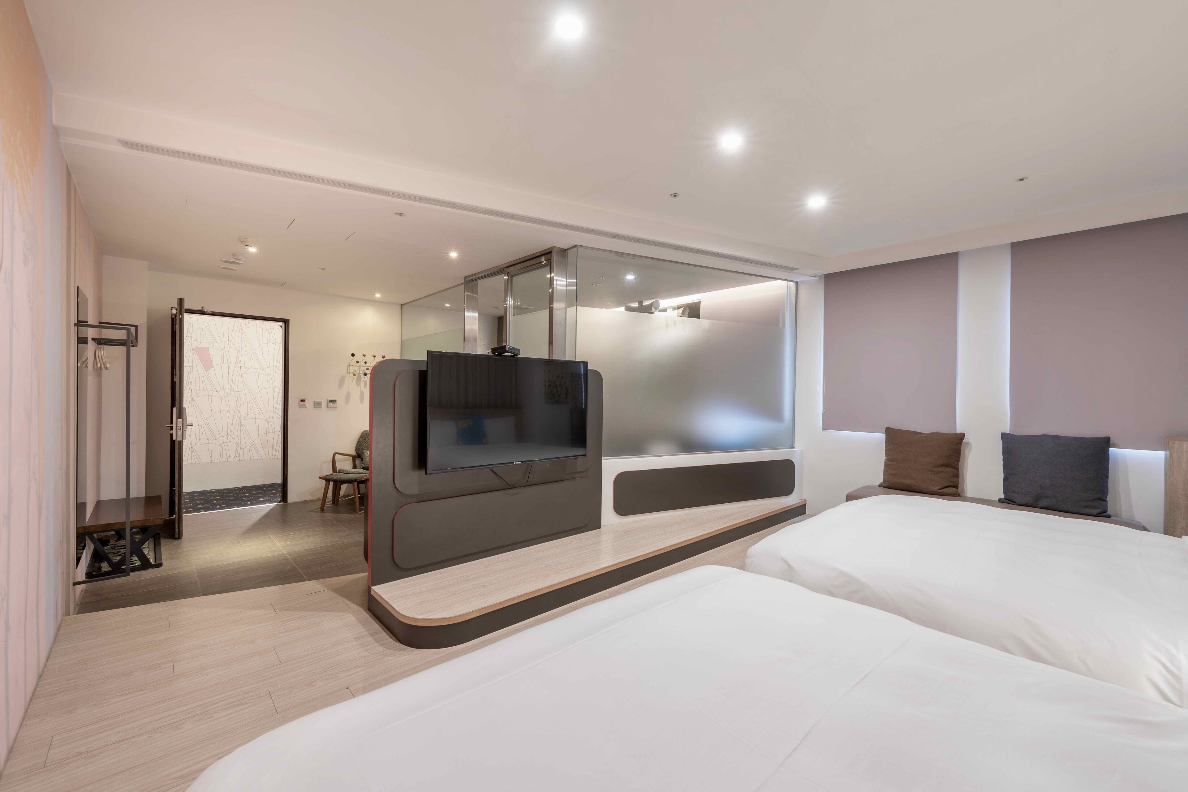 Une chambre d’hôtel moderne dotée d’un grand lit, d’un téléviseur fixé au mur, d’un coin salon et d’une cloison en verre.