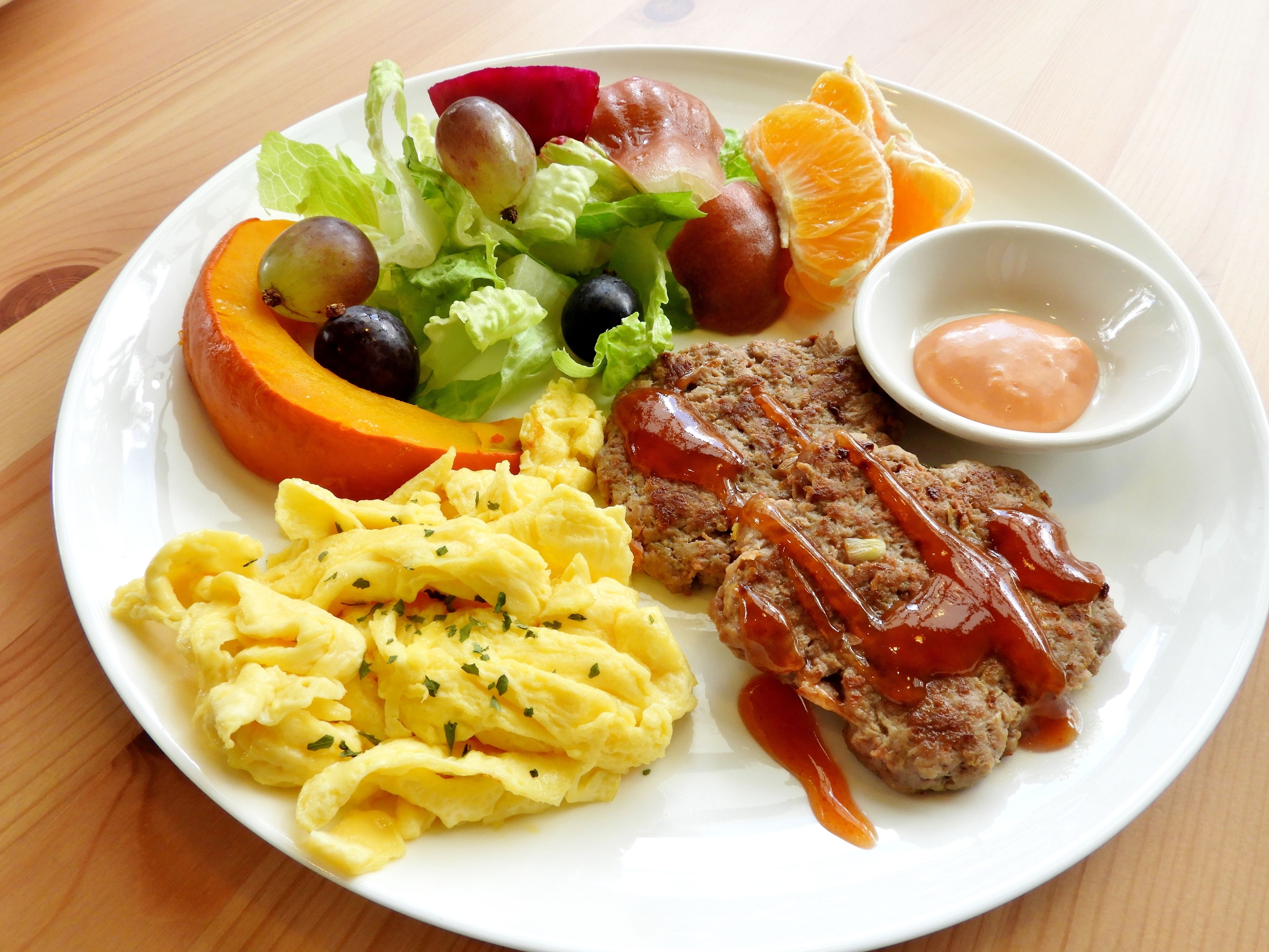 Un plato con huevos revueltos, una hamburguesa con kétchup, una rebanada de calabaza y una ensalada con diferentes verduras.