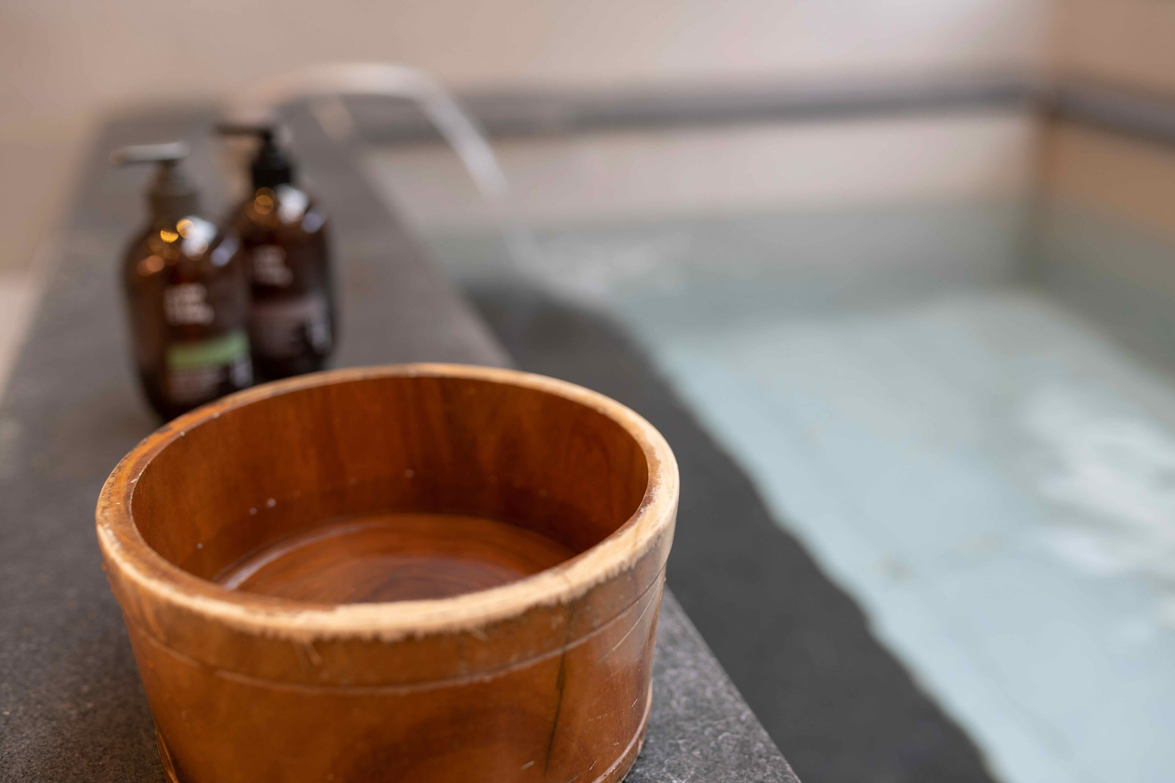 A wooden bowl on a stone ledge with a bathtub in the background.
