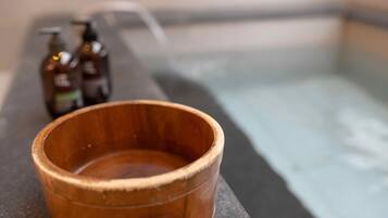 A wooden bowl on a stone ledge with a bathtub in the background.