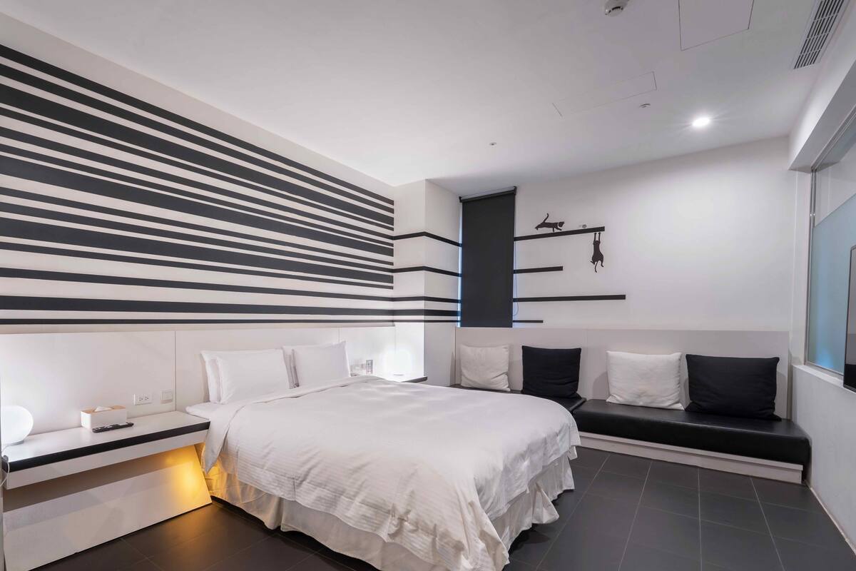 A modern bedroom with a large bed, bedside tables, a bench, and a wall with horizontal lines and animal silhouettes.