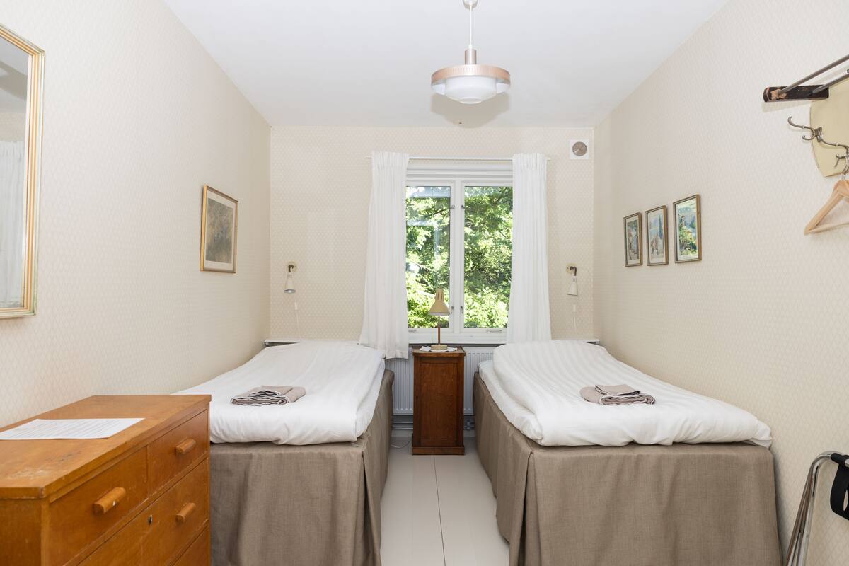 Een kamer met twee bedden, een houten dressoir, een radiator en een raam met gordijnen.
