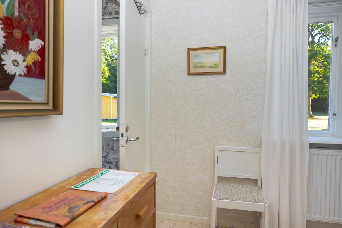 Een kamer met een houten bureau, een ingelijst schilderij, een wit schap en een deur die naar buiten leidt.
