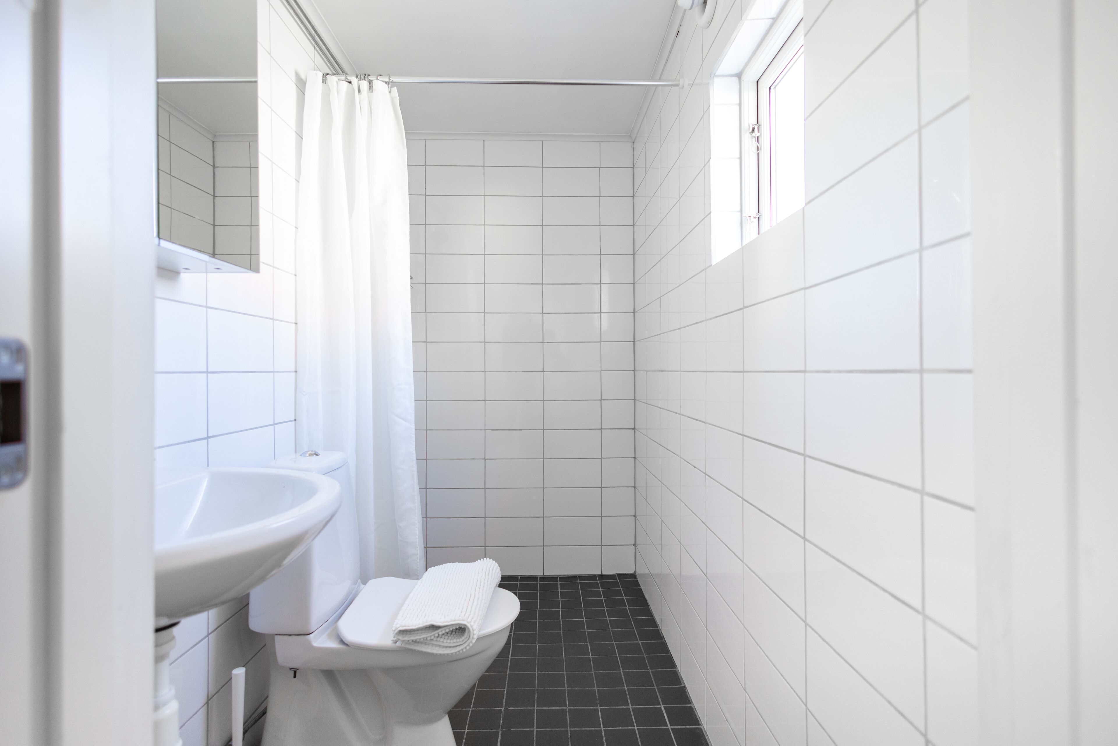 A small, narrow bathroom with white tiles, a white sink, a toilet, and a shower curtain.