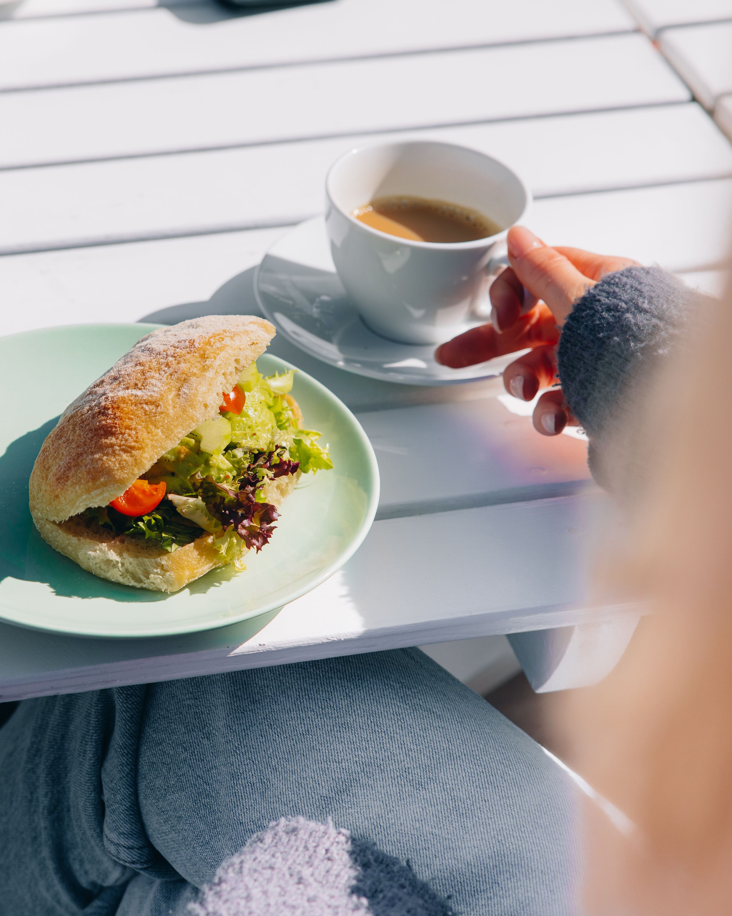Un sándwich en un plato con una taza de café sobre una mesa blanca.