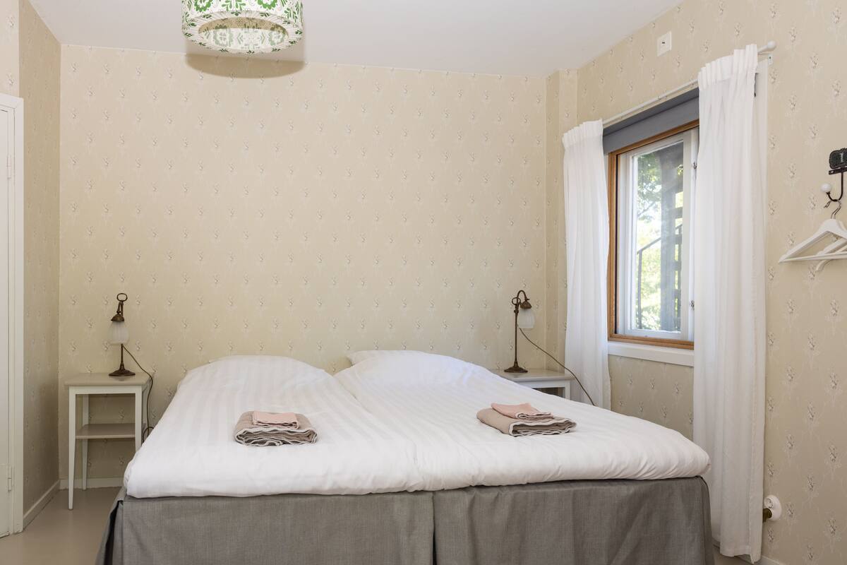 Een slaapkamer met een bed, twee nachtkastjes, een raam met gordijnen en een wandlamp.